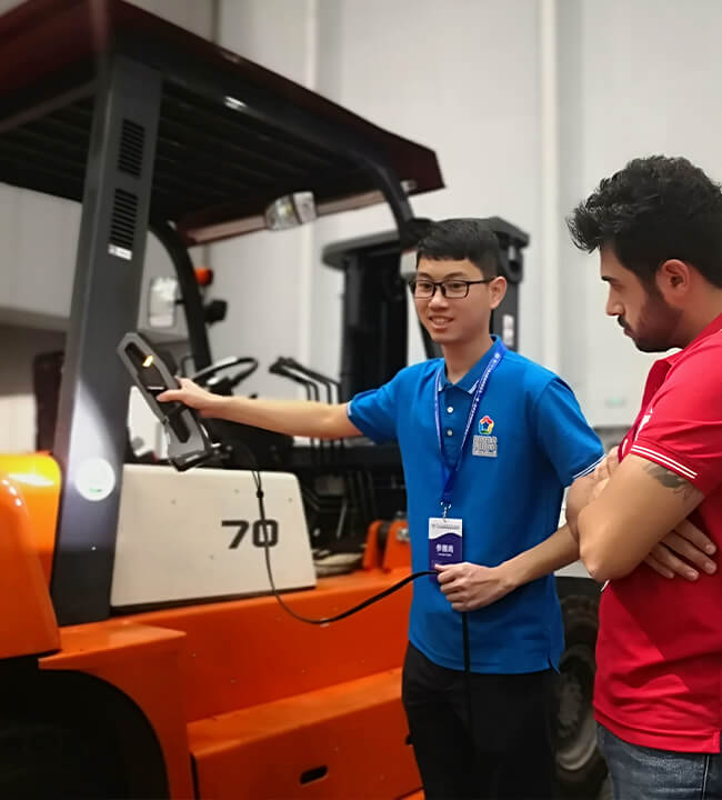 Technician demonstrating the use of a Creaform 3D scanner on an industrial forklift to a customer in a workshop setting.